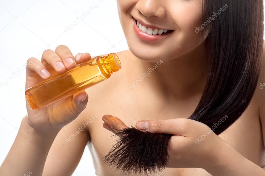 cropped shot of smiling woman pouring oil on split ends isolated on white