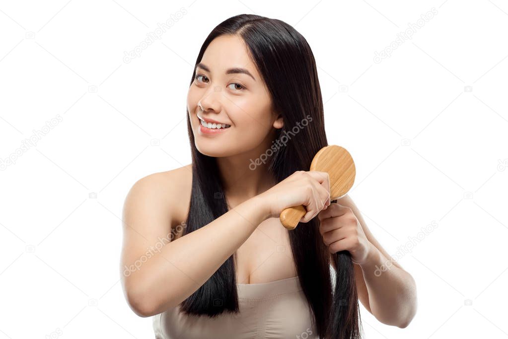 portrait of smiling beautiful asian woman brushing hair isolated on white