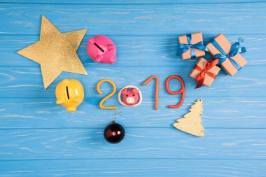 top view of piggy banks, christmas presents and 2019 symbol on blue wooden surface clipart