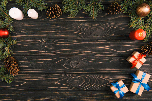 top view of christmas presents, candles and fir twigs with baubles and pine cones on wooden surface