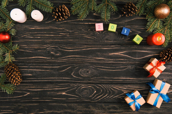 top view of 2019 symbol on cubes, christmas gifts, candles and fir twigs with baubles and pine cones on wooden surface