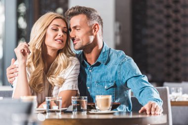 affectionate couple cuddling at table in cafe during date clipart