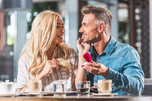 handsome boyfriend proposing surprised girlfriend and showing ring in cafe
