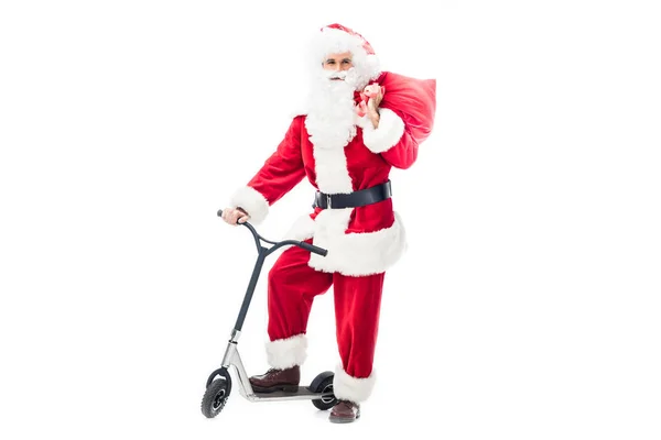 サンタ クロースの衣装はキック スクーターの上に立ってと 白い背景で隔離の肩越しにクリスマス袋を保持で  — 無料ストックフォト