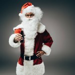 Smiling santa claus in costume standing with cream soda bottle isolated on grey background