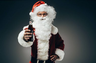 cheerful santa claus in costume showing cream soda bottle isolated on grey background  clipart