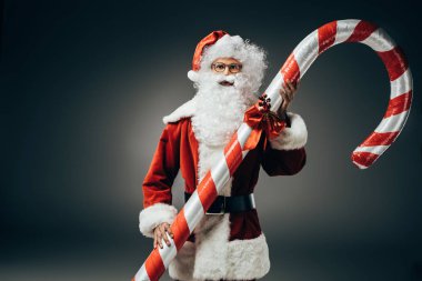 ciddi Noel Baba kostüm ayakta gri arka plan üzerinde izole büyük çizgili Noel sopa ile 