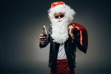 güneş gözlüğü ve kremalı soda şişe gösterilen ve gri arka plan üzerinde izole omuz üzerinde Noel ihale deri ceket şık Noel Baba 