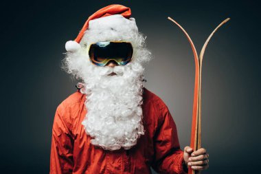 Noel Baba portresi kar maskesi ve gri arka plan üzerinde izole kayaklar ile ayakta rüzgarlık 