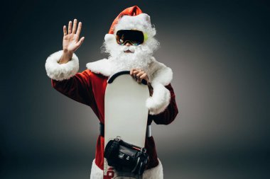 Noel Baba snowboard ile ayakta ve el sallayarak maske olarak gri arka plan üzerinde izole 