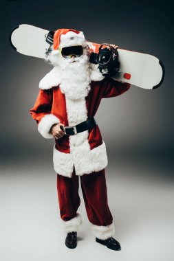 Noel Baba'ya kar maskesi gri arka plan üzerinde omuz üzerinden snowboard holding 