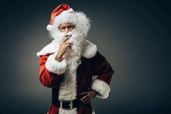 вдумчивый Санта-Клаус в костюме держась за руку у рта изолирован на сером фоне
 