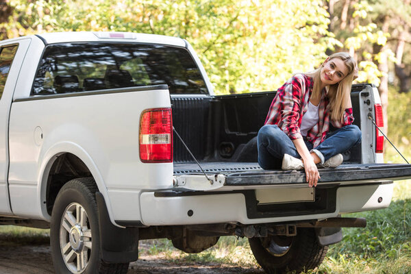 happy attractive woman sitting in trunk of pick up car outdoors 