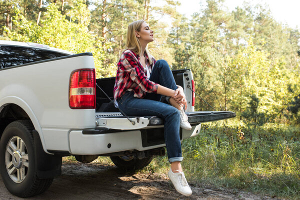 side view of young woman sitting in trunk of pick up car outdoors 