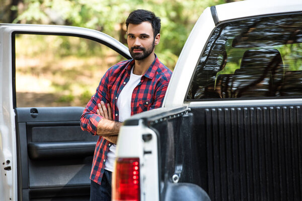 selective focus of young man standing with crossed arms near pick up car outdoors 