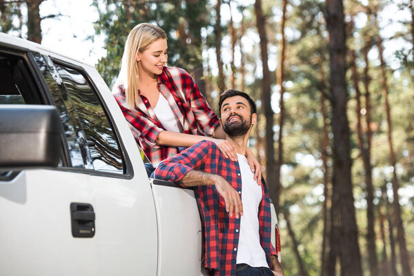 attractive young woman embracing boyfriend while sitting on pick up trunk outdoors 