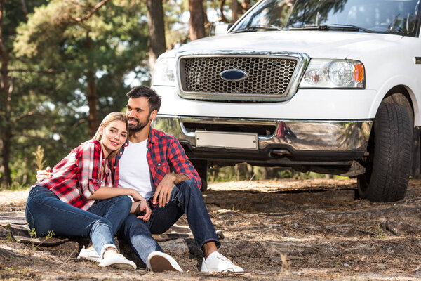 smiling young sitting on ground near pick up car in forest 
