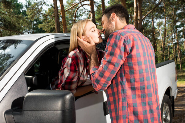 young man kissing attractive girlfriend sitting in pick up car outdoors 