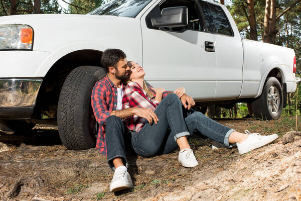 happy young couple sitting on ground and embracing near pick up car outdoors 