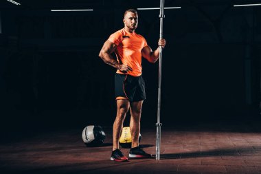 yakışıklı atletik sporcu ayakta ile bar-koyu spor salonu ve kameraya arıyor