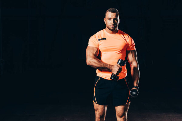 handsome athletic sportsman working out with barbells in dark gym