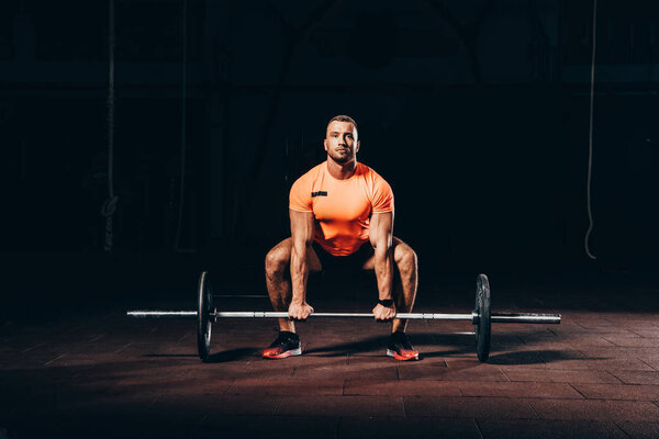 handsome athletic bodybuilder lifting barbell in dark gym