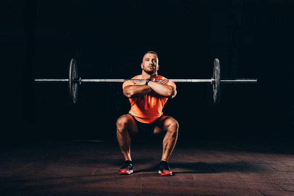 handsome muscular man doing squats with barbell in dark gym