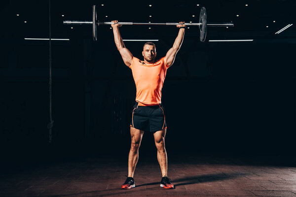 handsome muscular man working out with barbell in dark gym