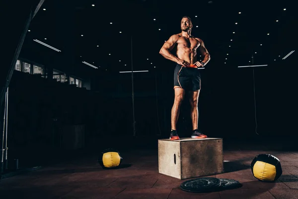 赤裸上身运动运动员站在立方体在黑暗的健身房和看远 — 图库照片