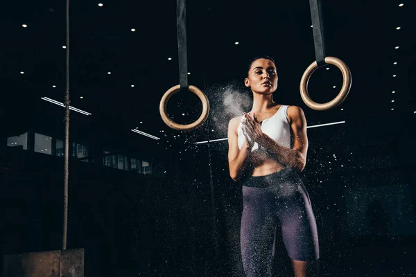 attractive sporty woman clapping hands with talc before workout with gymnastic rings