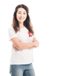 Happy adult asian woman with aids awareness red ribbon on t-shirt looking at camera with crossed arms isolated on white