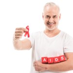 Hombre maduro feliz en blanco camiseta blanca con SIDA conocimiento cinta roja y bloques con letras de SIDA aislado en blanco