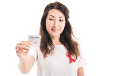 Yetişkin Asyalı kadın ile AIDS bilinçlendirme kırmızı şerit üzerinde beyaz izole t-shirt holding prezervatif üzerinde gülümseyen