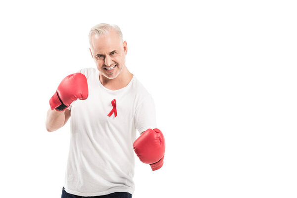 angry mature man in blank white t-shirt with aids awareness red ribbon and boxing gloves isolated on white, fighting aids concept