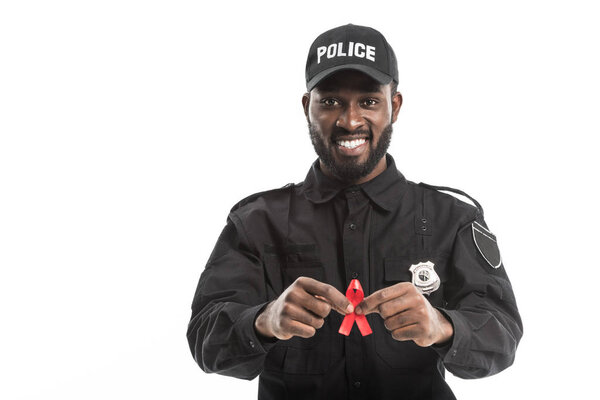 happy african american police officer with aids awareness red ribbon isolated on white
