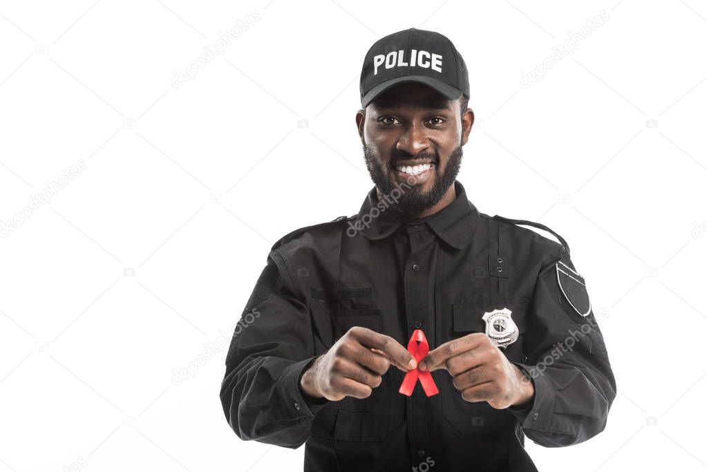 happy african american police officer with aids awareness red ribbon isolated on white