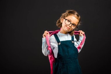 portrait of adorable schoolgirl in eyeglasses with backpack isolated on black clipart