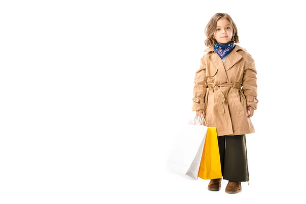 Bedårande Elegant Barn Trenchcoat Med Färgglada Shoppingkassar Tittar Kameran Isolerad — Gratis stockfoto