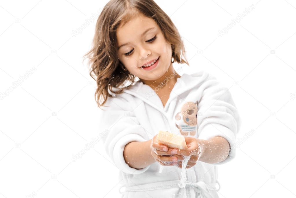 portrait of smiling kid in bathrobe washing hands with soap isolated on white