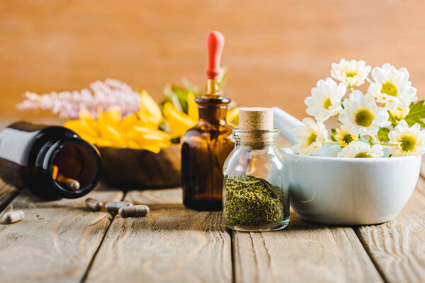 bottles of essential oils and herbs on wooden tabletop, alternative medicine concept