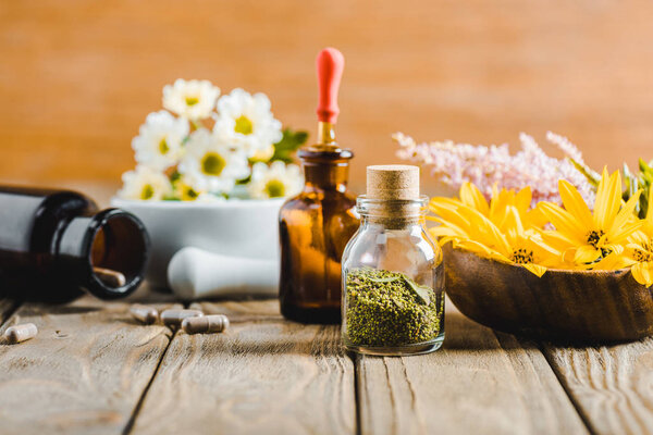 bottles of essential oils and blooming flowers on wooden tabletop, alternative medicine concept
