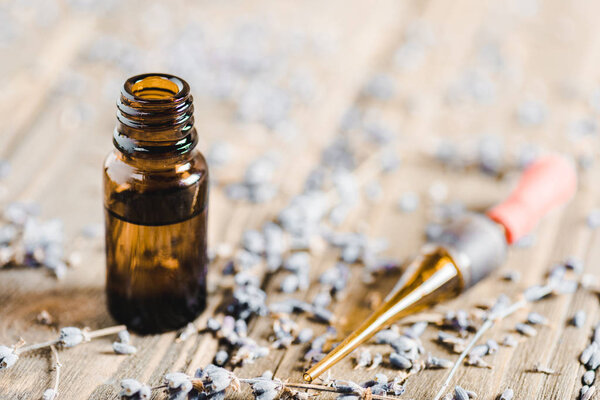 bottles of essential oil, dropper and scattered herbs on wooden tabletop, alternative medicine concept