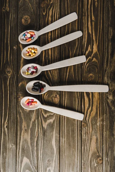 Vista Elevata Cucchiai Con Pillole Colorate Tavolo Legno — Foto stock gratuita