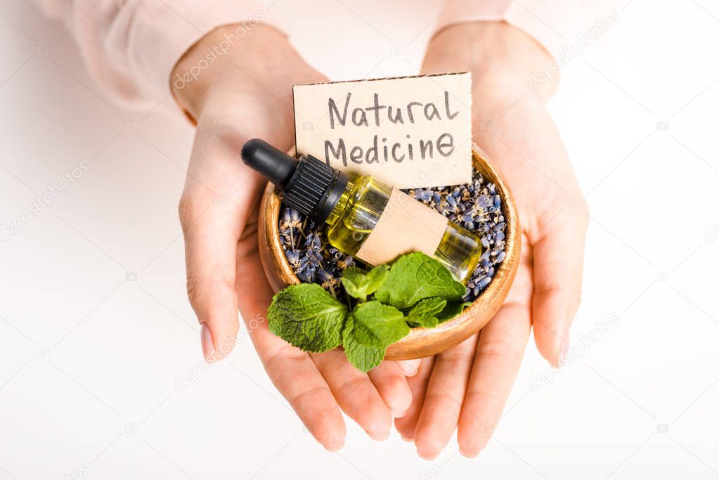 cropped image of woman holding bowl with essential oil and natural medicine sign isolated on white