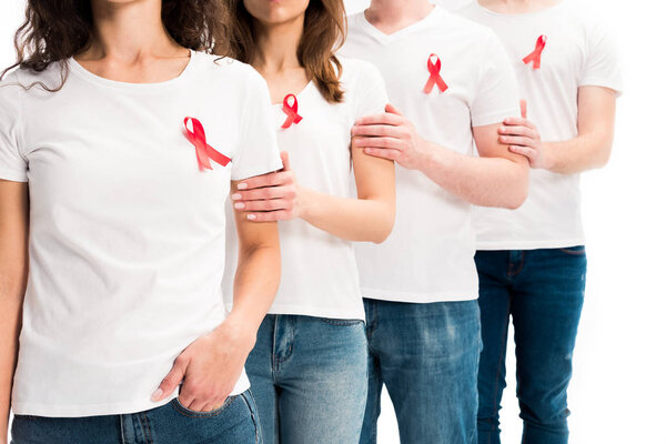 cropped image of people touching each other and standing with red ribbons on shirts isolated on white, world aids day concept
