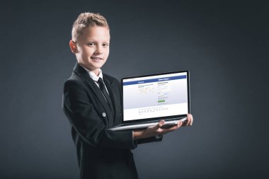 Web sitesi facebook ile dizüstü bilgisayar ekranında gri arka plan üzerinde gösterilen işadamı takım boy gülümseyerek
