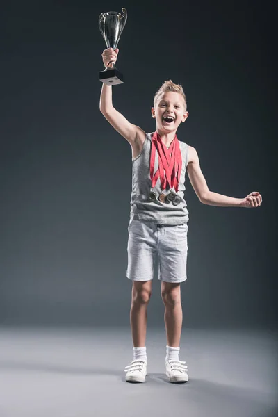 Щасливий Хлопчик Спортивному Одязі Медалями Кубком Чемпіонів Жестикулює Темному Фоні — стокове фото