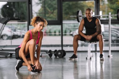 dantel bağlıyor ve kamera arkasında spor salonunda oturan erkek süre bakarak sporcumuz seçici odak