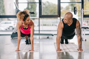 Afrika kökenli Amerikalı çift birbirine bakarak ve tahta spor salonunda fitness paspaslar üzerinde yapıyor sporcuların gülümseyen