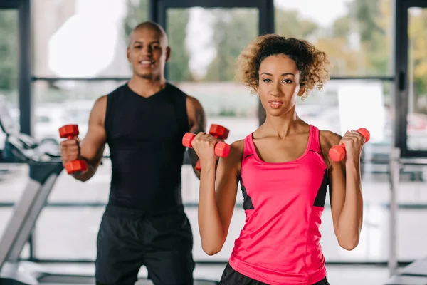 Onun Erkek Arkadaşı Arkasında Spor Salonunda Eğitim Sırasında Dumbbells Ile — Ücretsiz Stok Fotoğraf